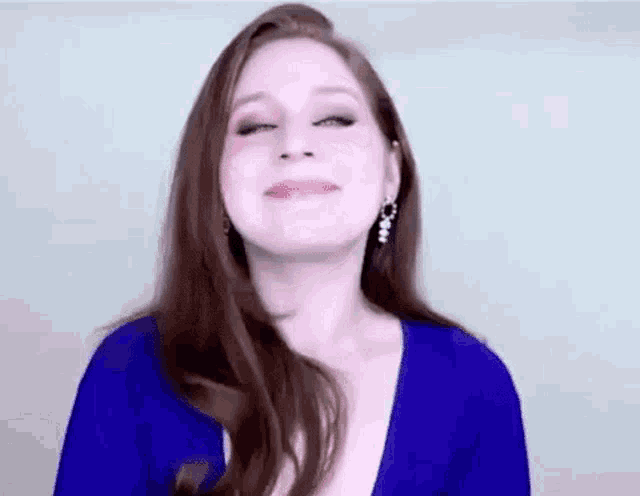 a woman wearing a blue top and earrings is smiling and looking at the camera .