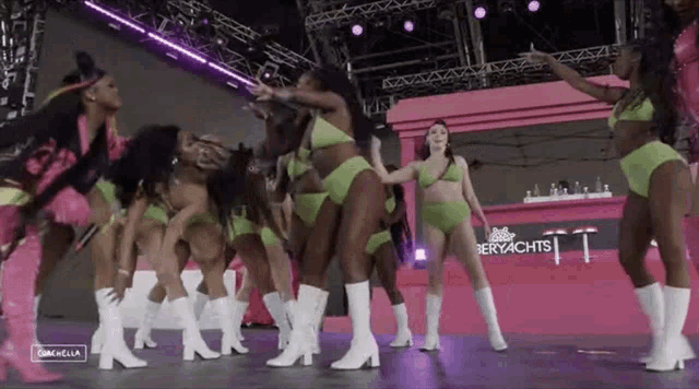 a group of women in green bikinis and white boots are dancing