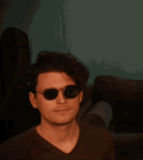 a man wearing sunglasses is sitting on a couch and holding his fist up .