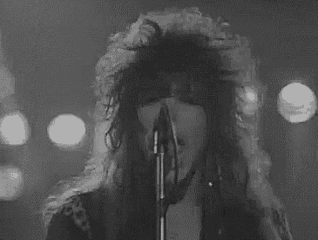 a black and white photo of a woman singing into a microphone with smoke coming out of her hair .