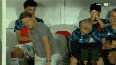 a group of soccer players sitting in a locker room with the number 1 on the bottom right