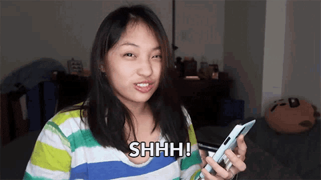 a woman in a striped shirt is holding a cell phone and says shhh