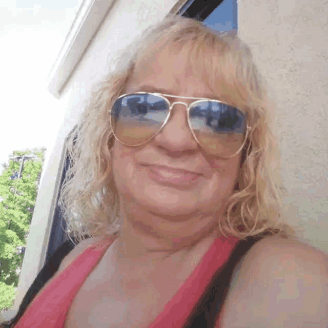 a woman wearing sunglasses and a pink shirt is smiling for the camera .