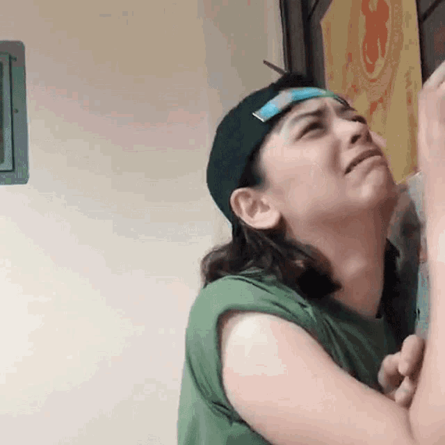a woman wearing a baseball cap and a green tank top is crying