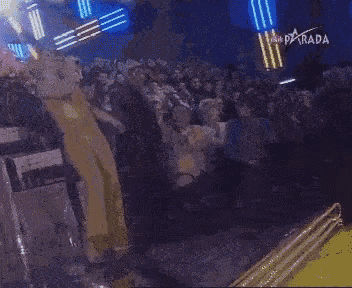 a woman in a yellow jumpsuit is dancing in front of a crowd with parada written on the bottom right