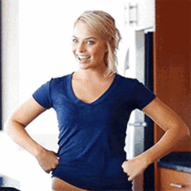 a woman wearing a blue shirt is standing in a kitchen with her hands on her hips .
