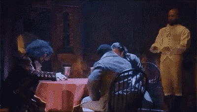 a group of men are standing around a table with a red table cloth .