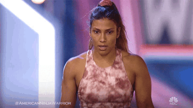 a woman in a pink tank top is standing in front of a sign that says american ninja warrior