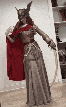 a woman in a costume with a red cape is holding a long sword