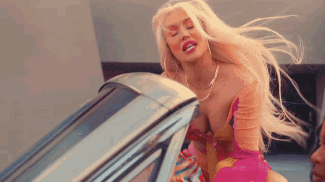 a woman in a pink and yellow dress is sitting in a car
