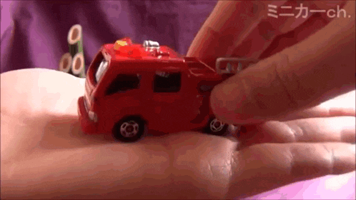 a person is holding a small red toy fire truck in their hand
