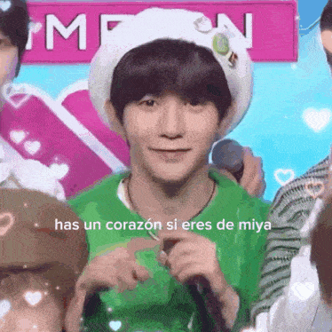 a young man wearing a hat and a green shirt is holding a microphone and says has un corazón si eres de miya