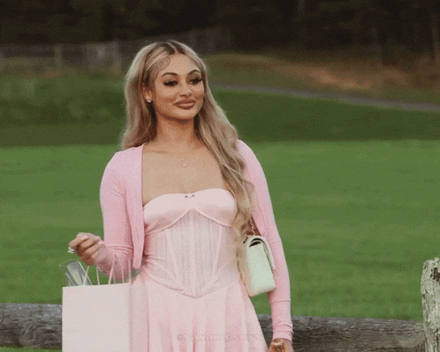a woman in a pink dress is holding a pink gift bag