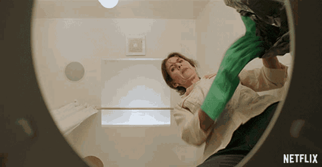 a woman wearing green gloves is cleaning a bathroom with a netflix logo in the background