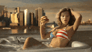 a woman in a bikini is holding a hamburger in her hand