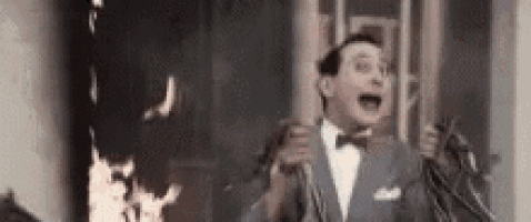 a man in a suit and bow tie is standing in front of a burning building .