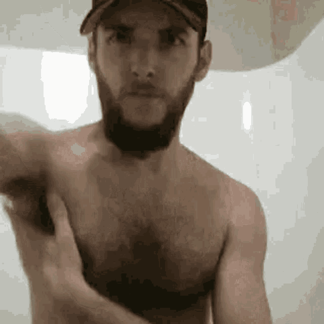 a shirtless man with a beard is taking a shower and washing his armpit .
