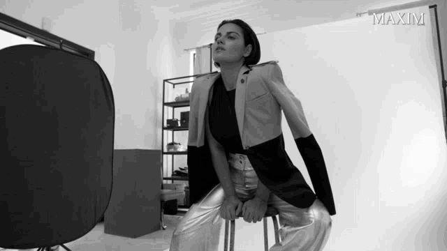 a black and white photo of a woman sitting on a stool with the word maxim on the bottom