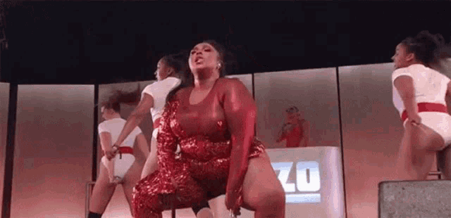 a woman in a red sequined dress is dancing on a stage with other women .