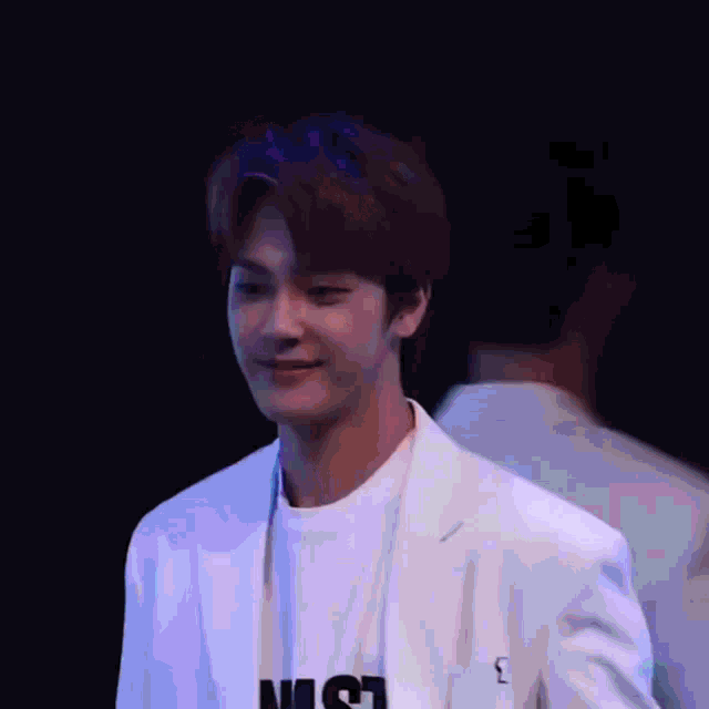 a young man wearing a white jacket and a white shirt is standing in front of a blue screen .