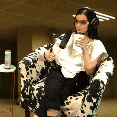 a woman wearing headphones is sitting in a chair holding a cup and a microphone