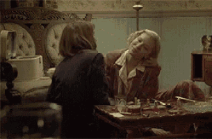 two women are sitting at a table in a room talking to each other .