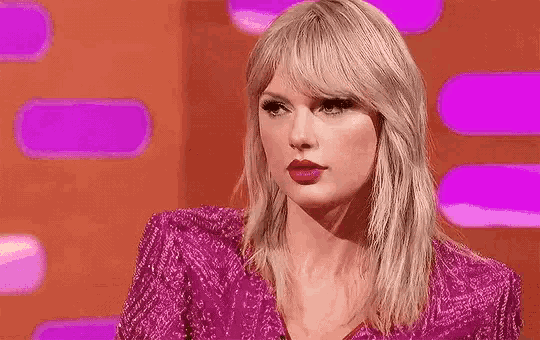 taylor swift is wearing a pink dress and making a funny face while sitting on a stage .