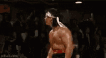 a man with a bandage on his head is running in a boxing ring with the words e 37 anos caralho behind him .