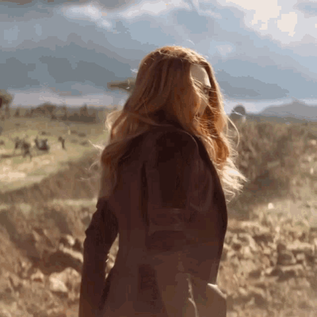 a woman with long red hair is walking in a field