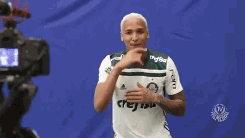 a man in a green and white shirt is standing in front of a camera and smiling .