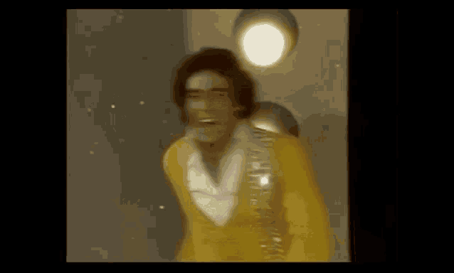 a man in a yellow jacket is dancing in front of a group of lights .