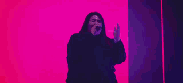 a woman is singing into a microphone in front of a pink background that says la batalla d fe