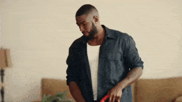 a man in a black shirt is standing in a living room holding a red hose .