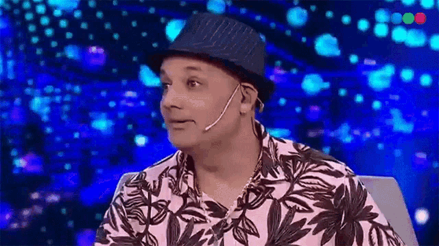 a man wearing a hat and a pink shirt is sitting in front of a microphone on a stage .