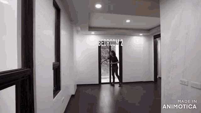 a woman is opening a sliding glass door in an empty room with the words bedroom 2 on the wall .