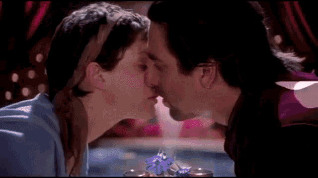 a man and a woman are kissing in front of a glass of flowers .