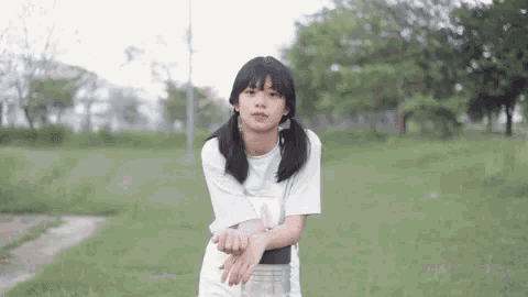 a girl in a white t-shirt is standing in a field with her hands folded