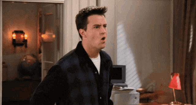 a man in a plaid shirt is standing in a room with his mouth open .