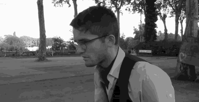 a man wearing glasses and a vest is standing in a park