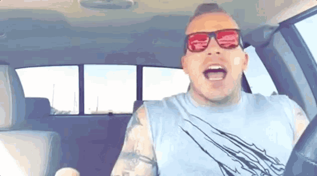 a man wearing sunglasses and a blue tank top is singing in a car