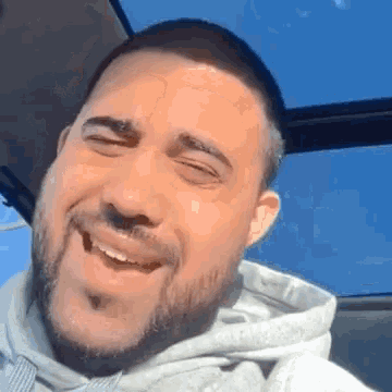 a man with a beard wearing a grey hoodie is smiling with his eyes closed