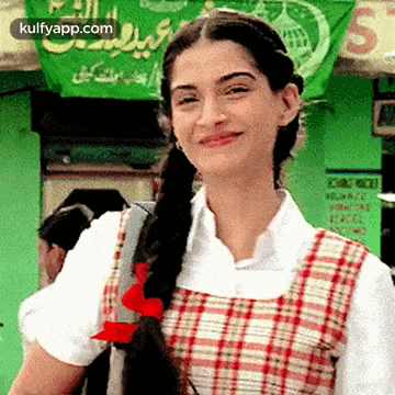 a woman in a plaid dress is smiling while standing in front of a green banner .