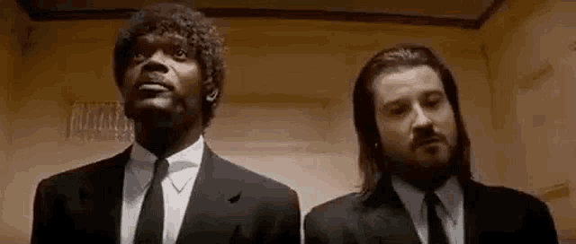 two men in suits and ties are standing next to each other in an elevator and looking up .