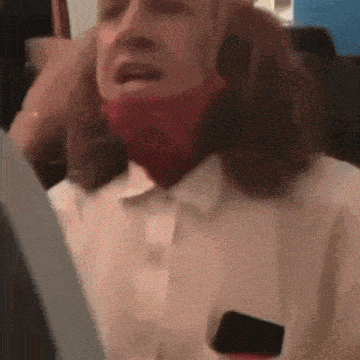 a woman wearing a red mask is crying on a plane while holding a cell phone .