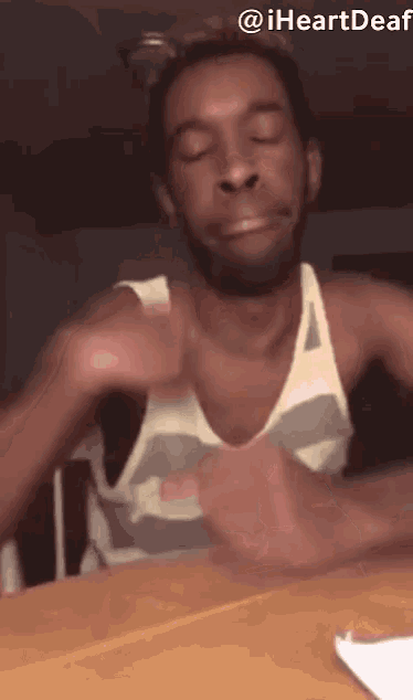 a man in a tank top is sitting at a table with his eyes closed and making a funny face .