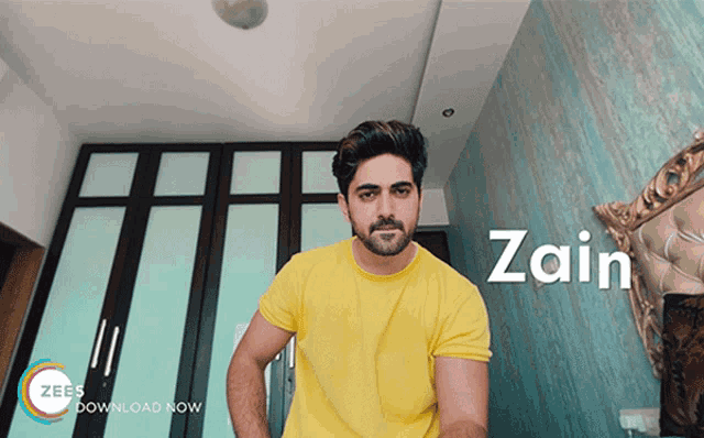 a man in a yellow shirt is standing in front of a wall with the word zain on it