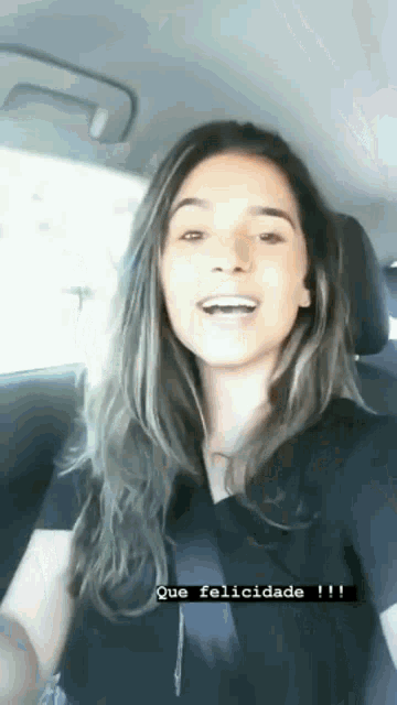 a woman is taking a selfie in the back seat of a car while wearing a black shirt and smiling .
