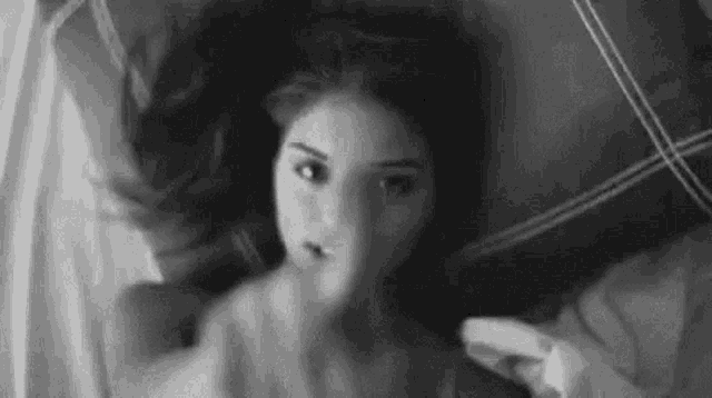 a black and white photo of a woman laying in bed .