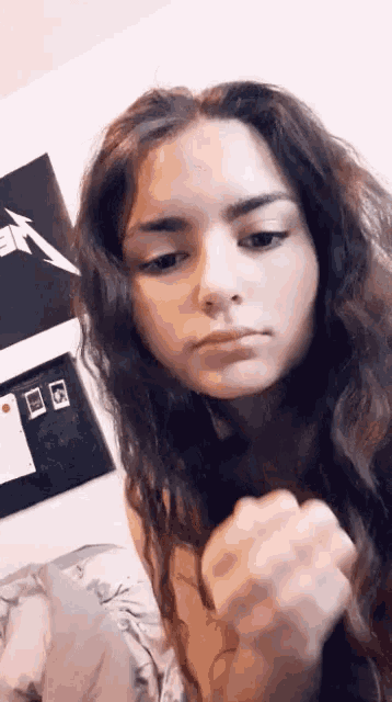 a girl with long hair is looking at the camera with a metallica poster in the background