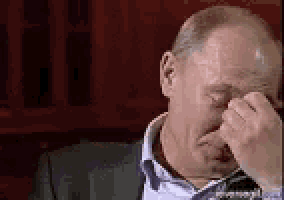 a bald man in a suit and tie is covering his face with his hand .